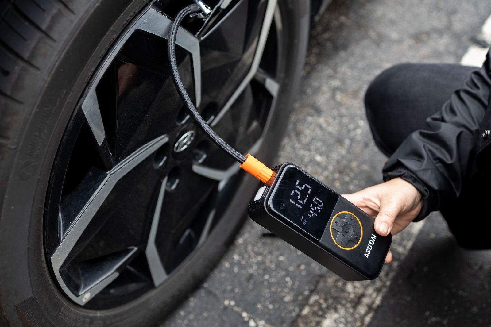 Compact portable tire inflator next to car wheel on driveway.