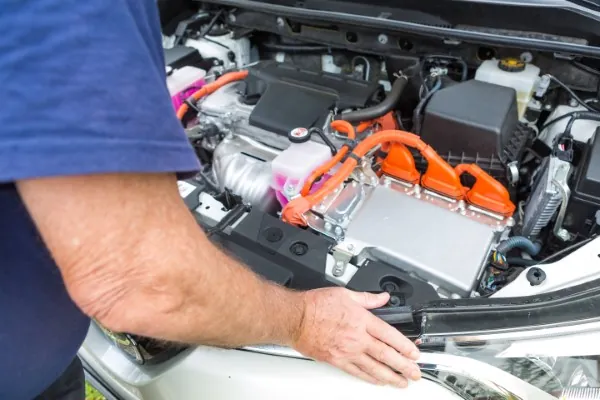 Hands checking tightness of car battery cable clamp during inspection.
